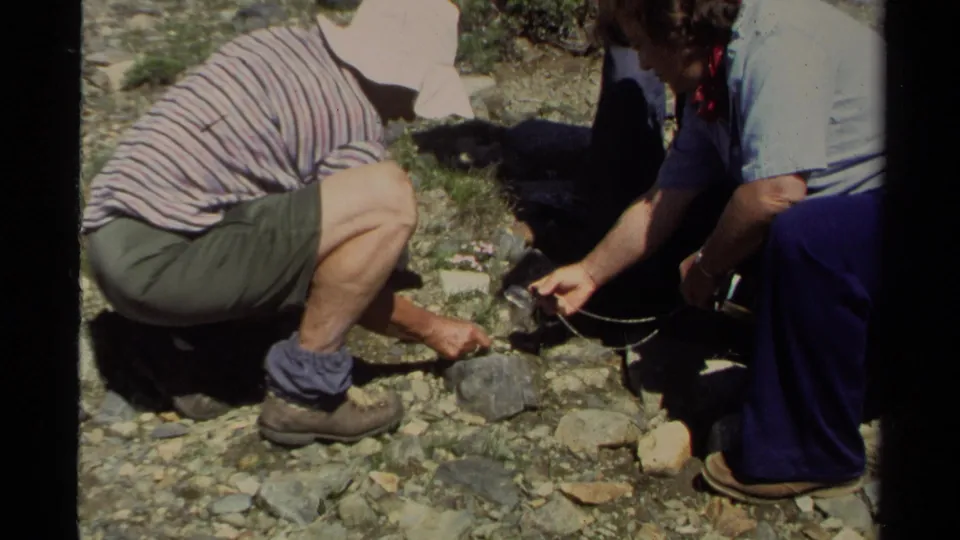Adults in 1978 Lake Tahoe footage crouch by a rock, with one person appearing to inspect it using a small magnifying glass or tool.