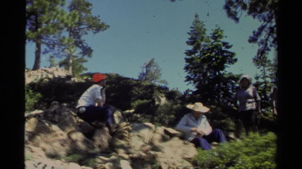 A wider 1978 Lake Tahoe view shows adults resting and standing among rocks, low brush, and pine trees under clear sky.