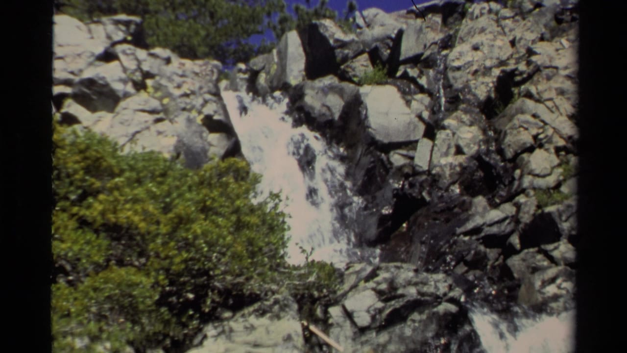 1978 Lake Tahoe home-movie frame showing a rocky waterfall, brush and a distant person standing above the rushing water.