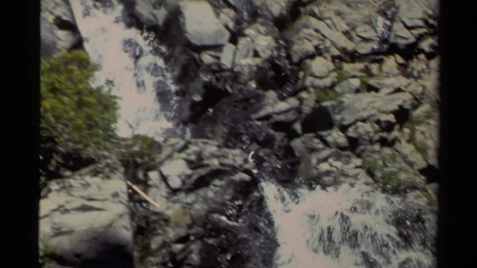 Lake Tahoe 8mm frame with white water cascading through gray boulders and green vegetation on a steep rocky slope.