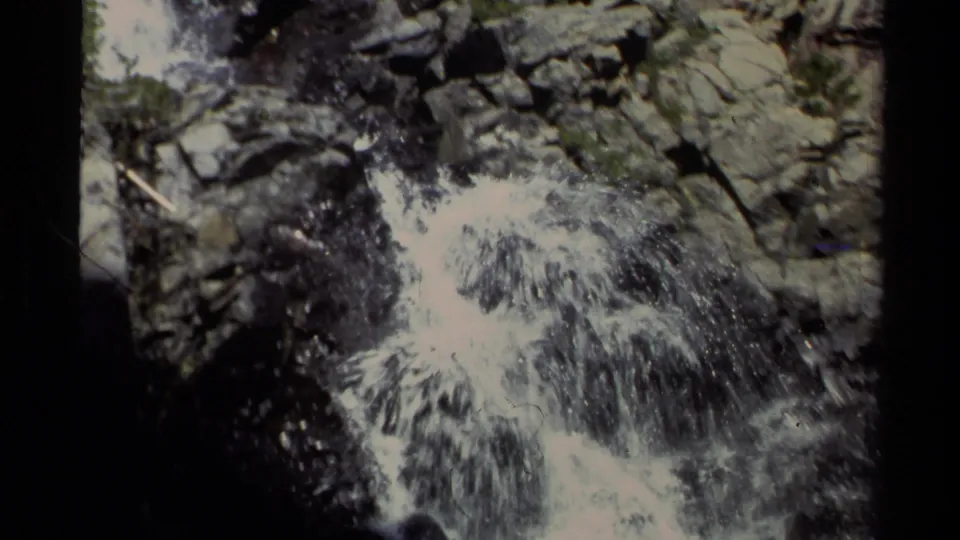 1978 Lake Tahoe home-movie frame showing foamy water spilling over layered rocks, with small shrubs around the cascade.