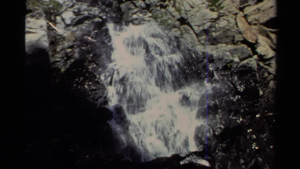 Lake Tahoe 8mm frame of bright white water cascading over gray boulders, framed by dark film edges and sparse greenery.