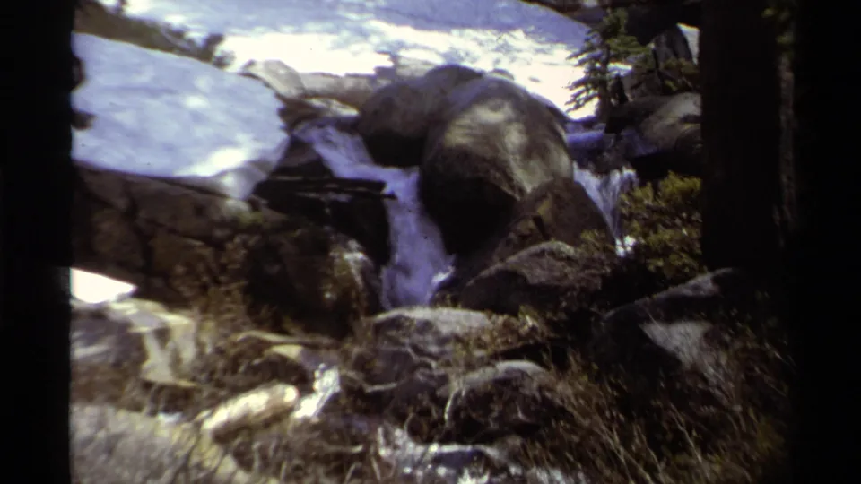 Handheld 8mm view of a rocky Lake Tahoe stream with snow, brush, and water moving through boulders.