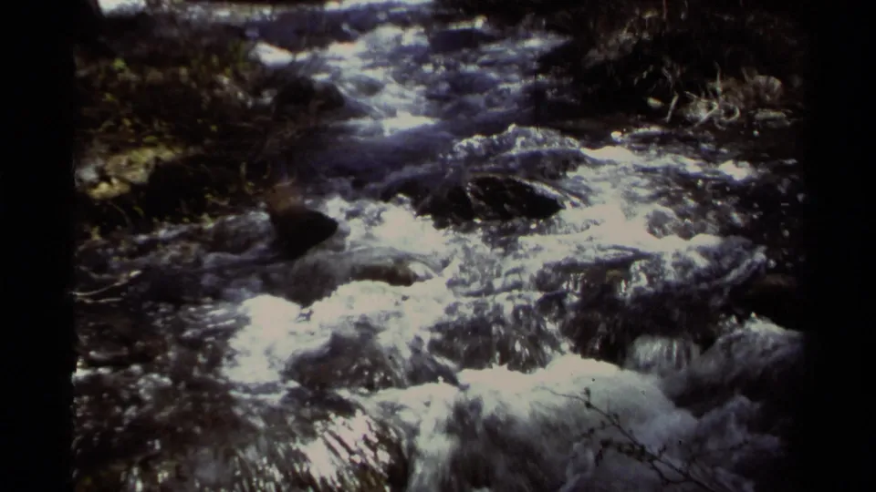1978 8mm Lake Tahoe frame showing foamy rapids dropping through a rocky creek bed with shaded vegetation nearby.