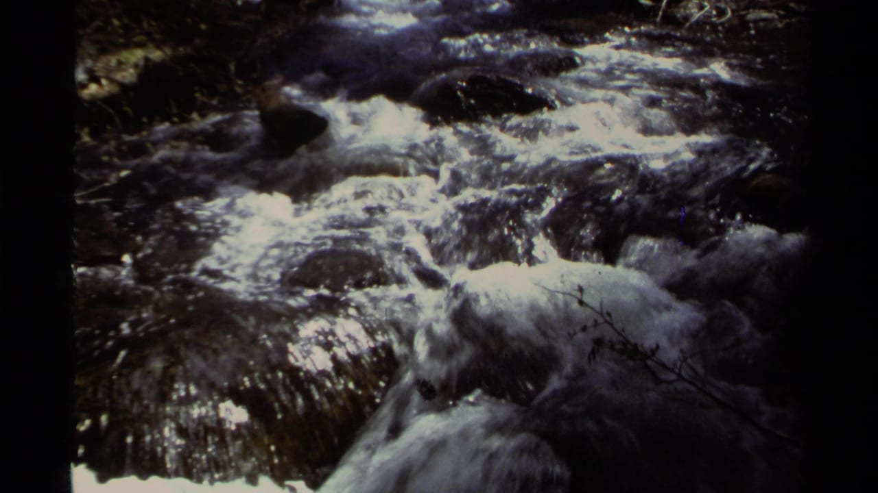 1978 Lake Tahoe 8mm frame showing fast white water flowing over dark rocks in dappled shade.