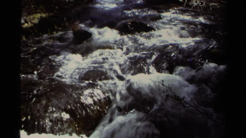 1978 Lake Tahoe 8mm frame showing fast white water flowing over dark rocks in dappled shade.