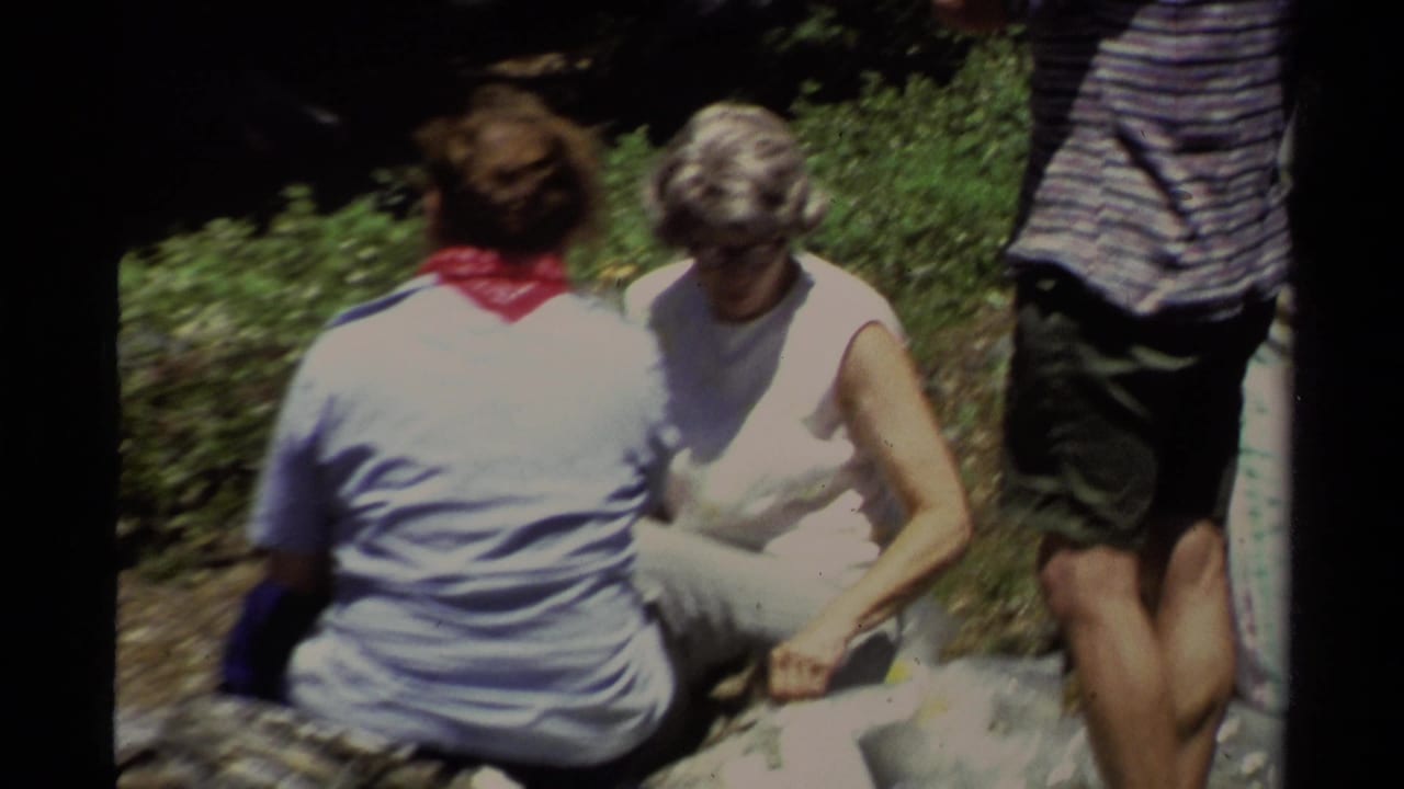 Adults gather around a sunny Lake Tahoe picnic spot, with one seated figure wearing a red bandana.