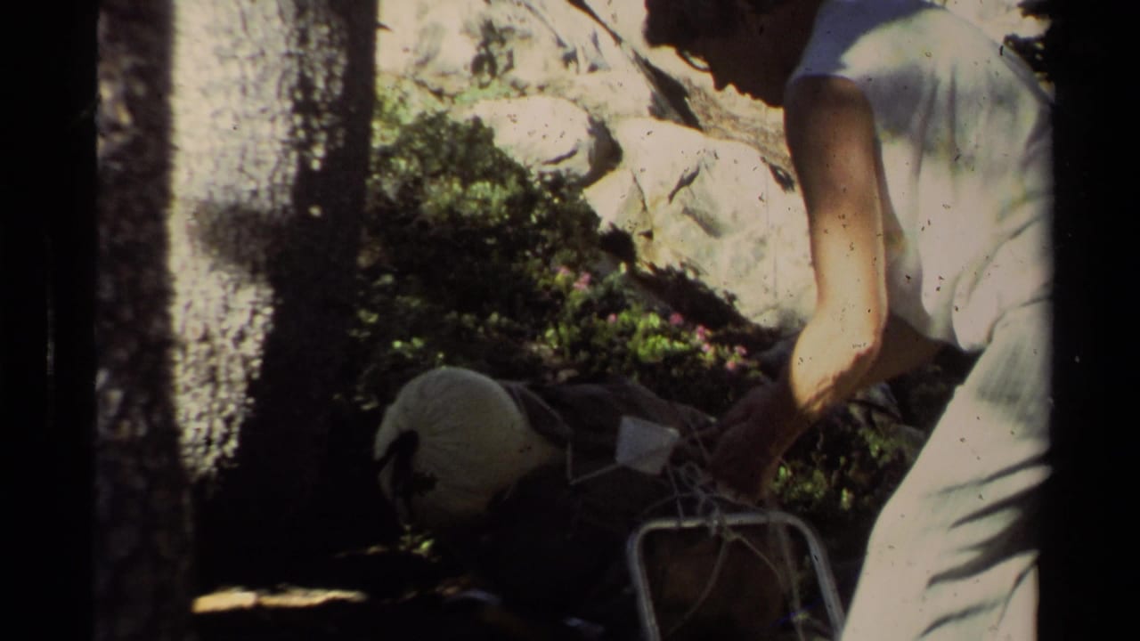 1978 Lake Tahoe home-movie frame with a hiker leaning over trail gear in a shaded pine and rock setting.