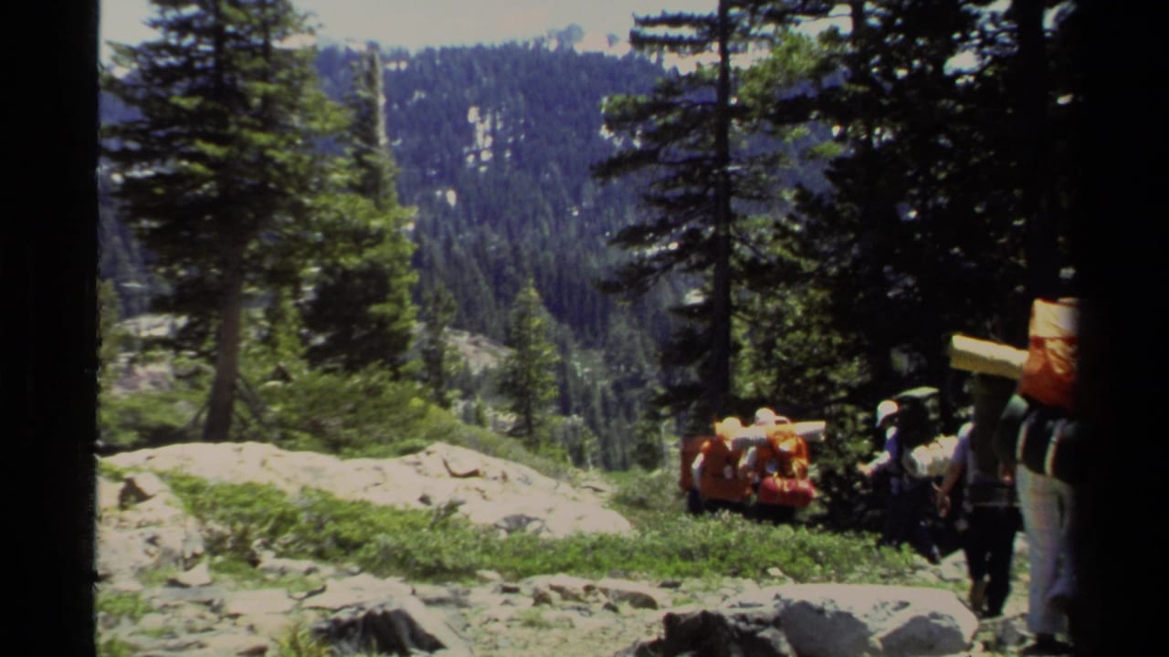 Lake Tahoe hikers in 1978 appear at the edge of frame with orange and dark packs beside trees and mountain terrain.
