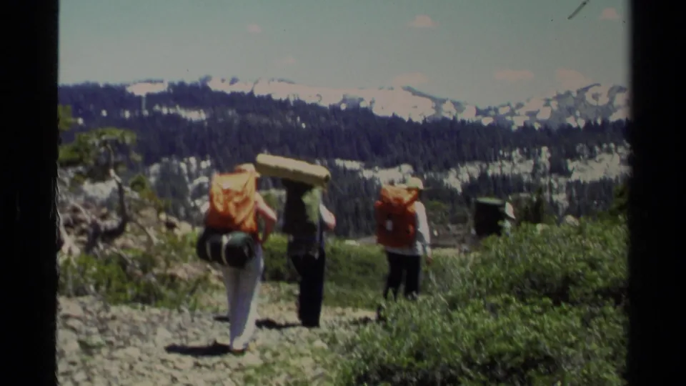 1978 Lake Tahoe 8mm view of backpackers descending a rocky alpine trail toward distant snow-covered peaks.