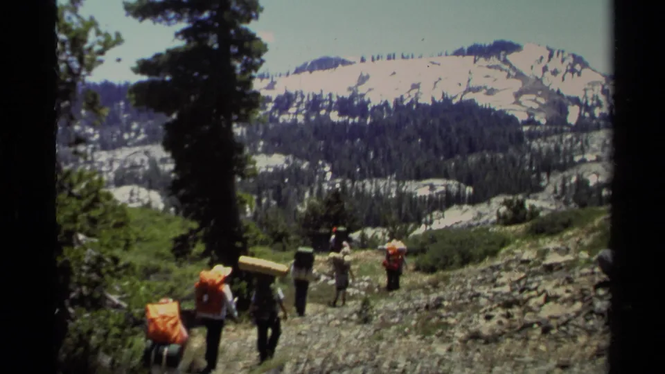 Group backpacking scene in Lake Tahoe, 1978, with hikers spread along a rocky alpine slope below snow-patched ridges.