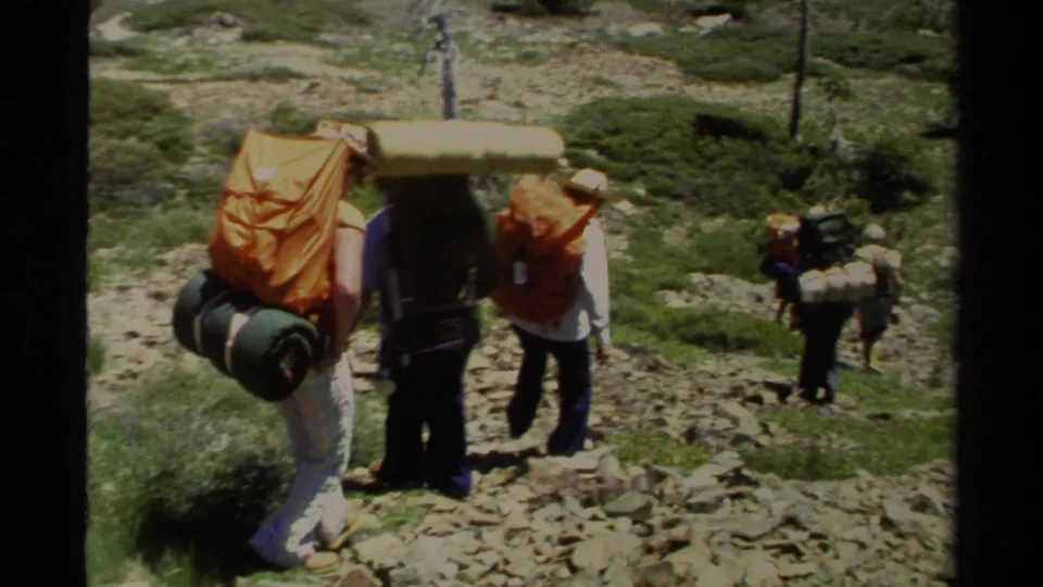 Lake Tahoe backpackers with large packs and sleeping mats move carefully downhill on a rocky alpine trail in 1978 footage.