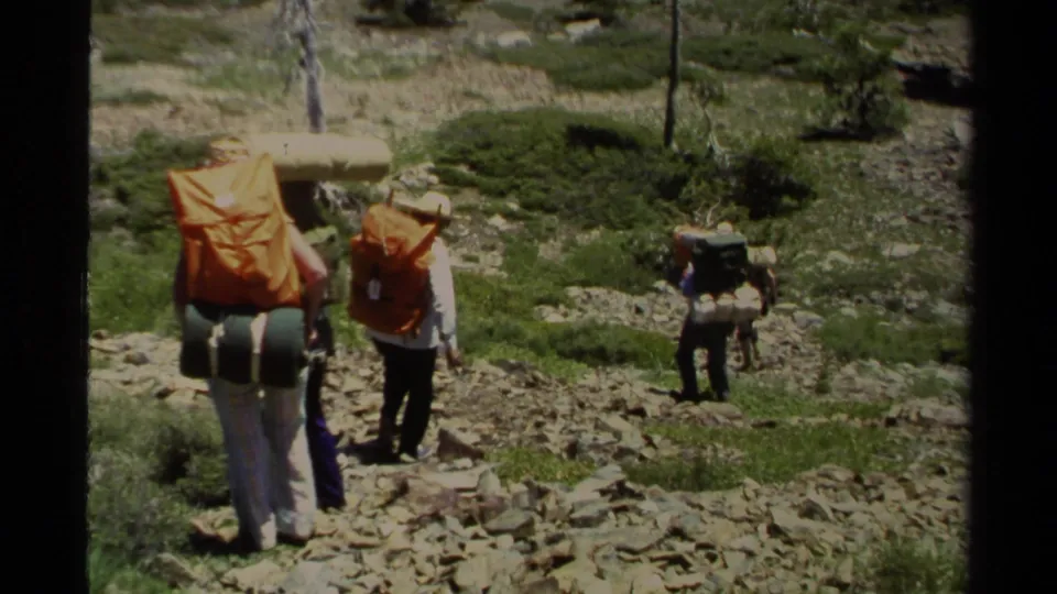 1978 Lake Tahoe trail scene with hikers carrying orange-covered packs and a separate backpacker farther down the rocky slope.