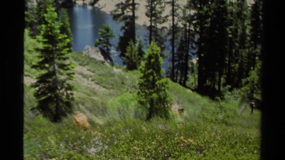 Lake Tahoe appears through tall evergreens, with blue water below a green hillside in 1978 home-movie footage.