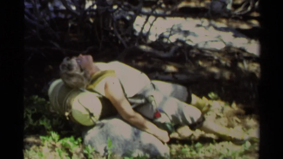 The woman remains reclined on rocky ground, partly in bright sun, with plants and tangled branches around her in the 1978 Lake Tahoe scene.