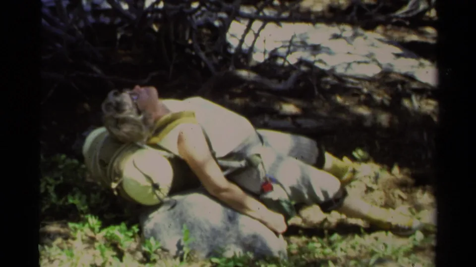 At Lake Tahoe in 1978, a woman lies on a rock with her head near a backpack amid shaded branches and green vegetation.