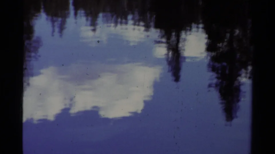 A 1978 Lake Tahoe water view shows broad cloud reflections and dark tree shapes wavering across the blue surface.