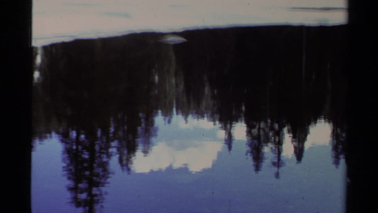 Lake Tahoe winter shoreline in 1978 home-movie footage, with snow and conifers reflected in still water.