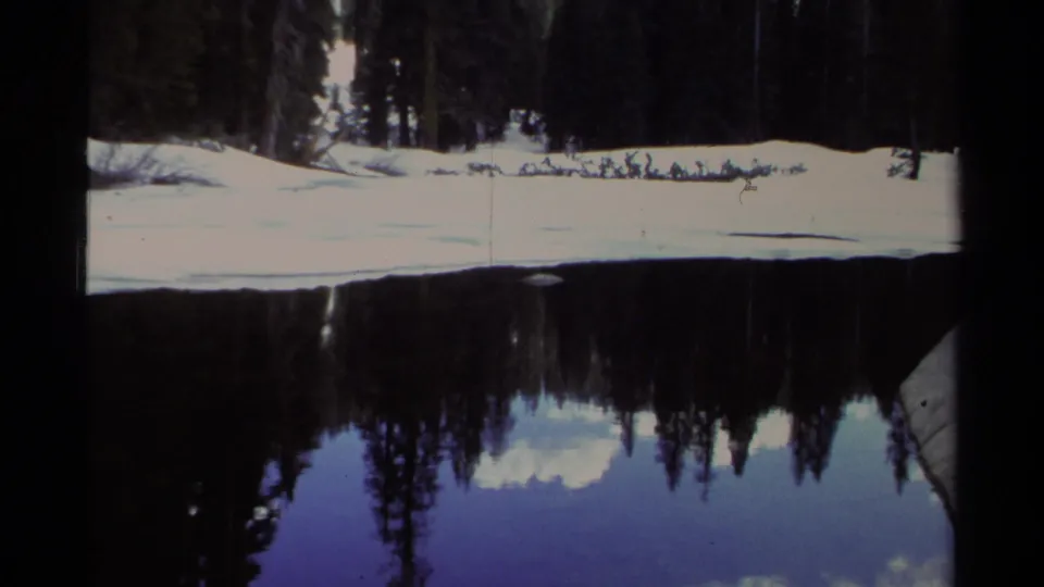 End frame of the 1978 Lake Tahoe winter reflection shot, showing snow, conifers, still water, and film-frame edges.