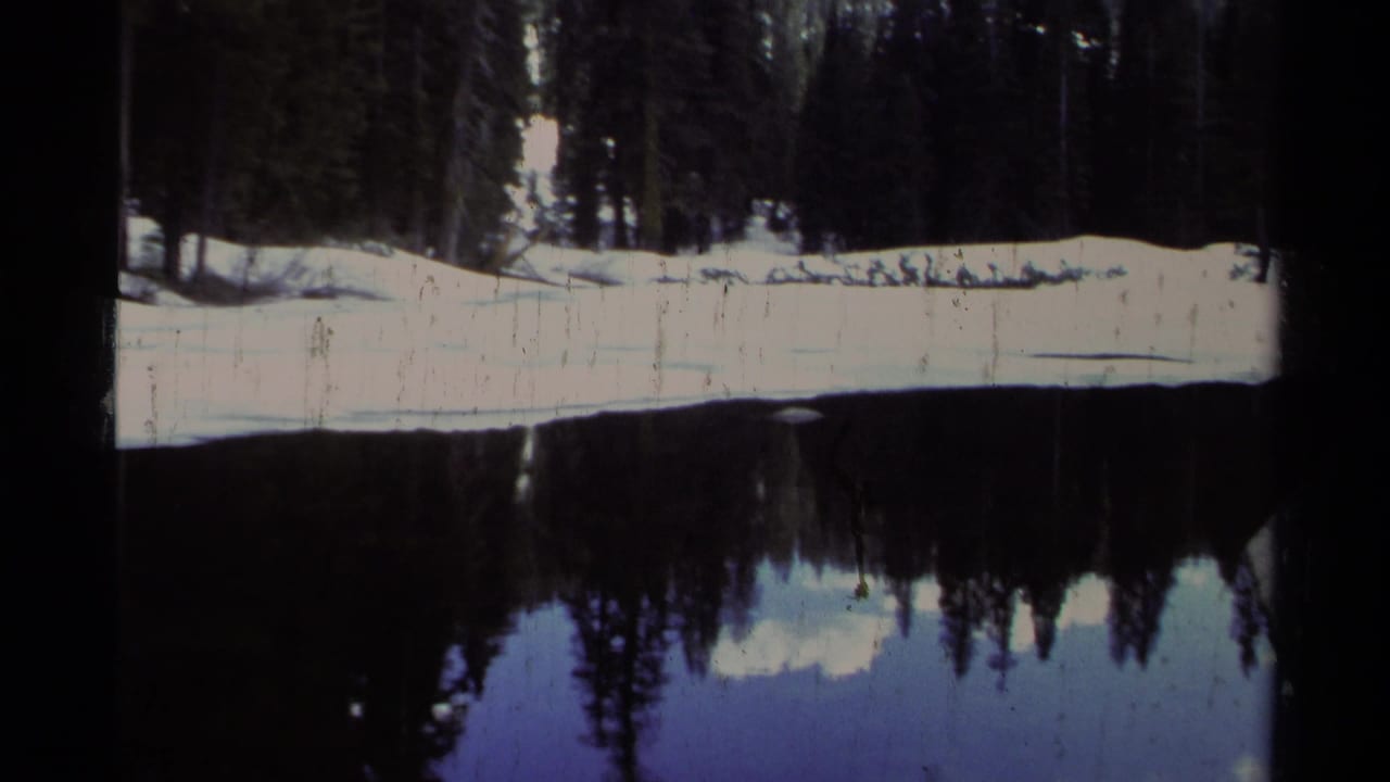 1978 Lake Tahoe 8mm frame showing snow along a forested lakeshore reflected in calm, dark water.