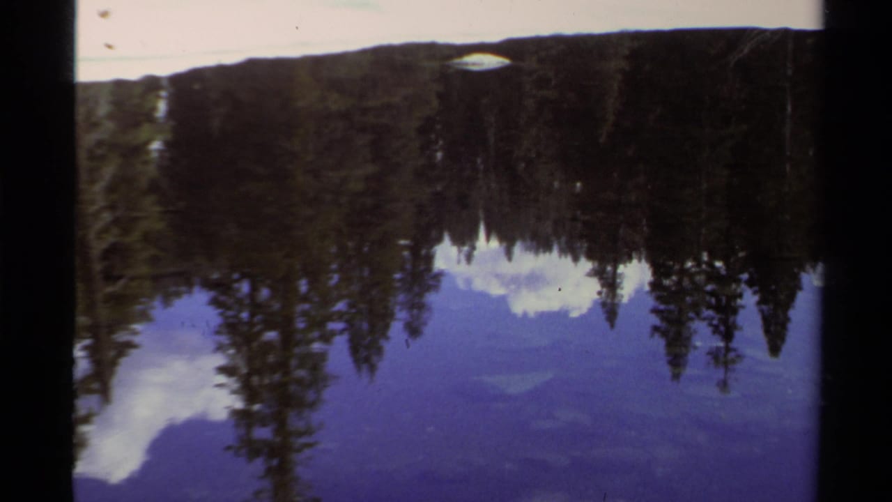 Reflected evergreen shoreline and clouds appear upside down across deep blue lake water.