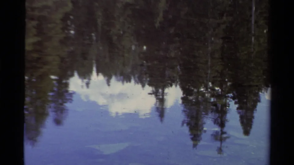 1978 Lake Tahoe frame during the zoom, showing reflected conifers and clouds softened by 8mm grain and color fading.