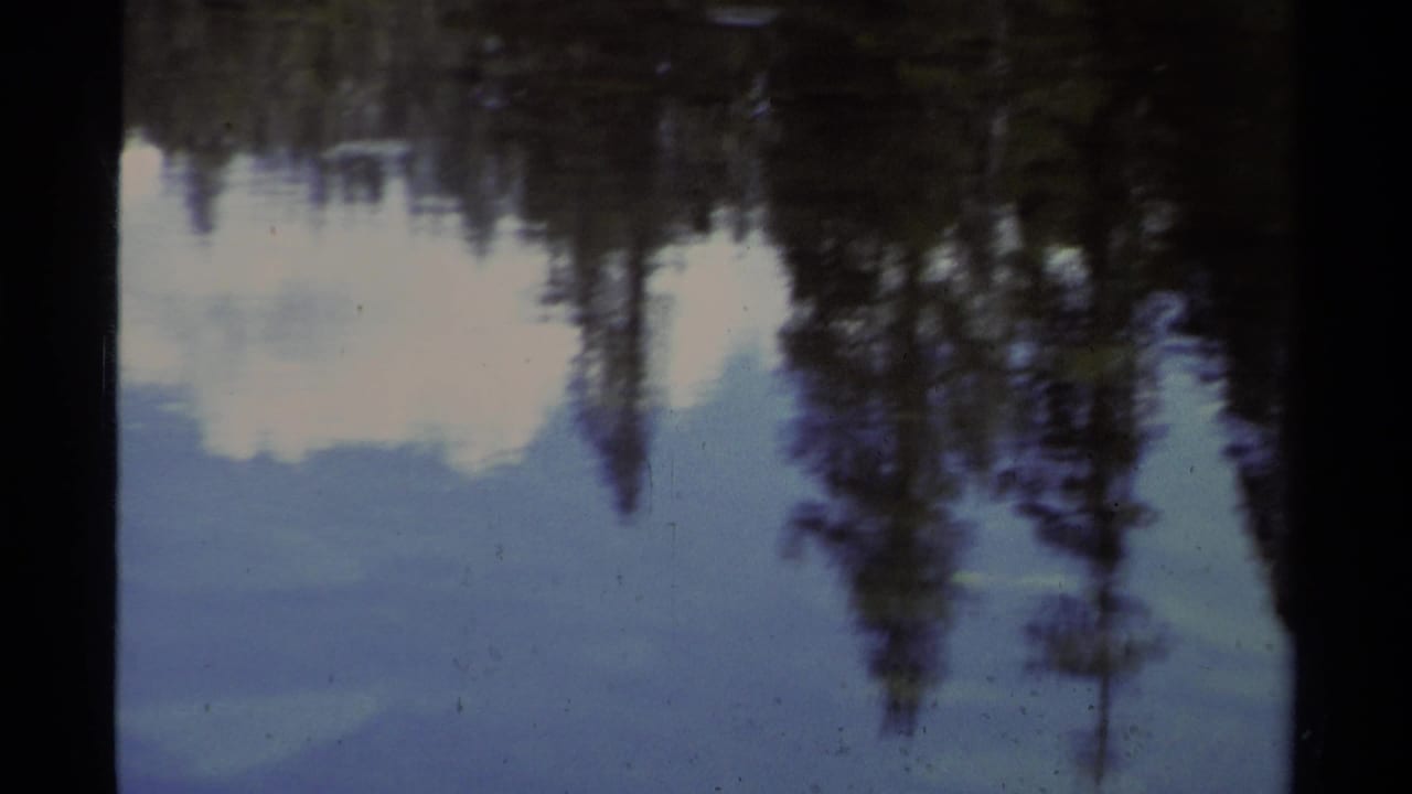 Lake Tahoe home-movie frame showing pine trees and sky reflected in still water, with soft 8mm exposure and dark frame borders.