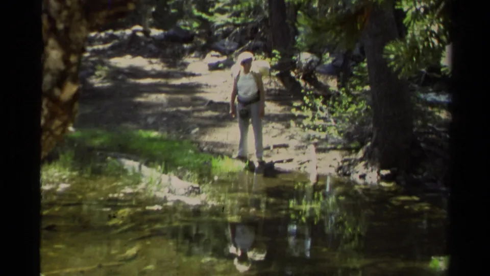 A zoomed 8mm view shows the adult man beside shallow lakeside water on a wooded Lake Tahoe path, framed by pine shade.