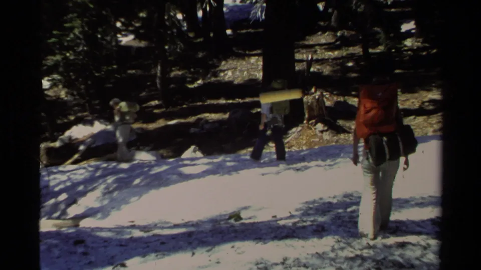Hikers carrying external-frame packs walk over patchy snow in the forest, consistent with the Lake Tahoe 1978 clip metadata.
