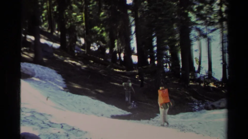 1978 Lake Tahoe 8mm frame showing two hikers in a snowy pine forest, with bright snow and deep tree shade.