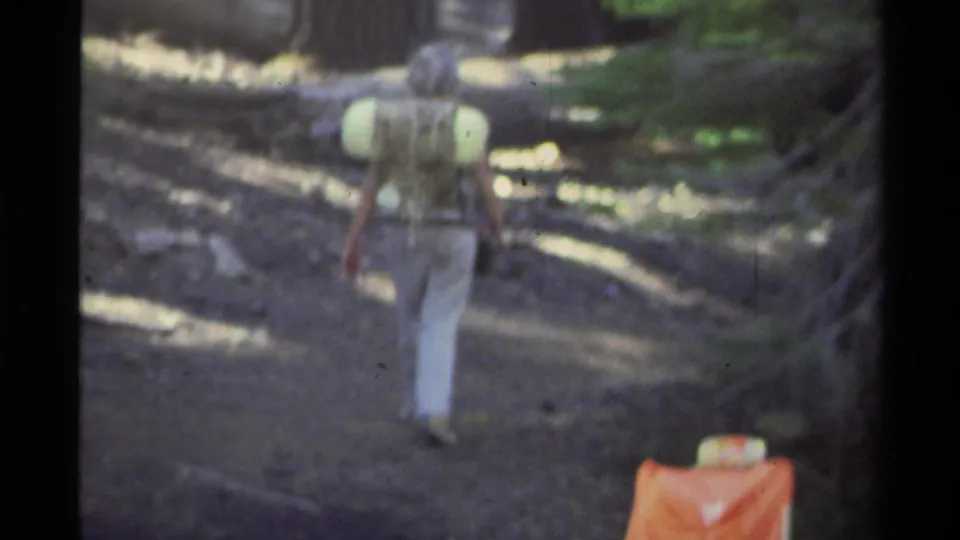 Soft 8mm frame from Lake Tahoe in 1978 showing a backpacked hiker walking away on a shaded forest trail.