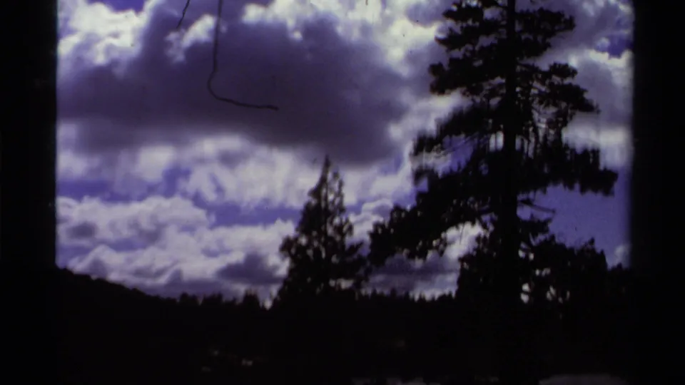 1978 Lake Tahoe home-movie frame with a tall pine and forest edge silhouetted against heavy clouds and blue-purple sky.