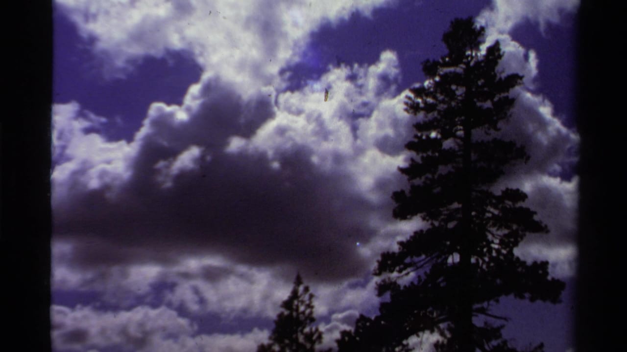1978 Lake Tahoe 8mm frame showing a tall pine at right against bright layered clouds and saturated blue-purple sky.