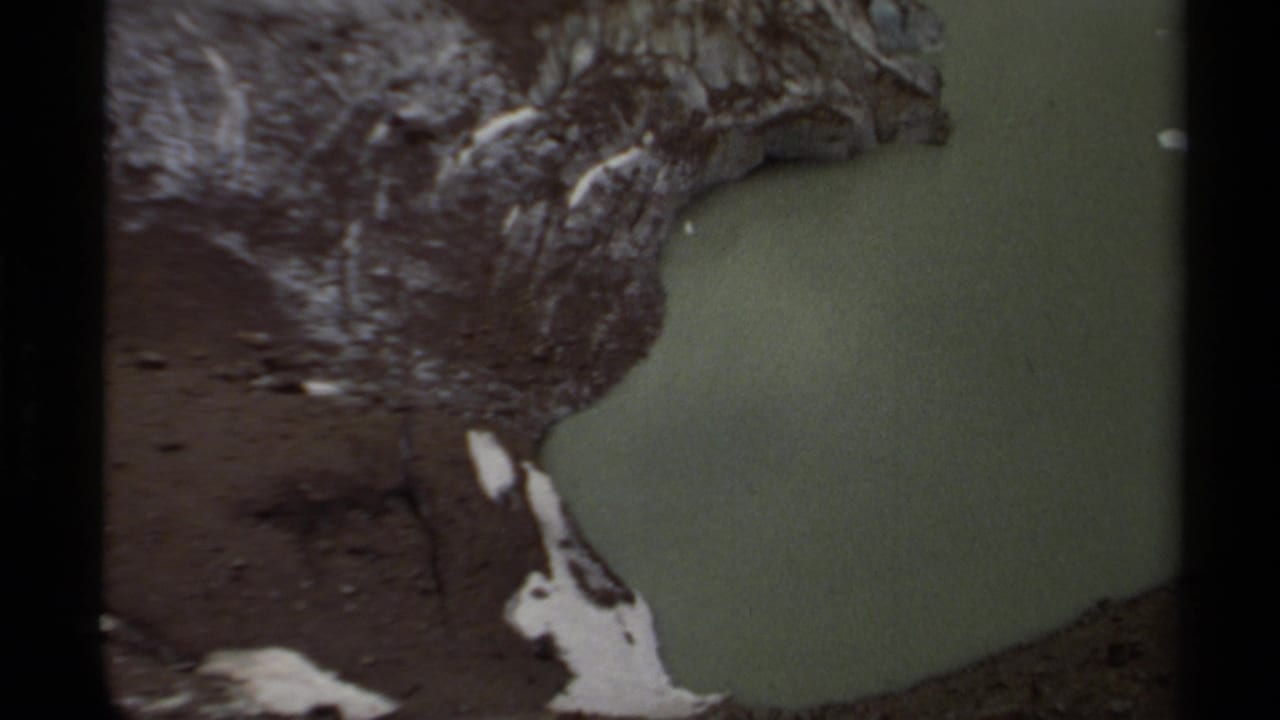 Greenish water pool bordered by dark rock and small snow patches.