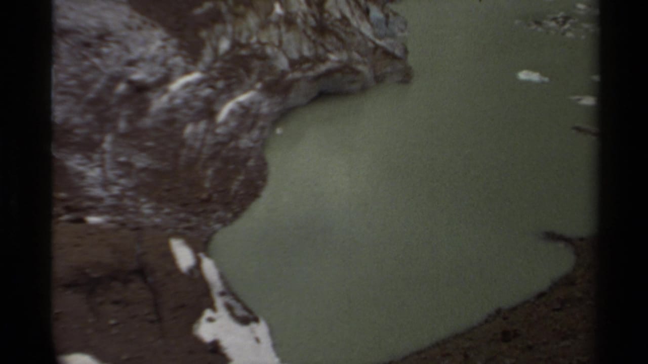 1979 British Columbia home-movie frame with a greenish pool enclosed by rocky slopes and lingering snow at the edge.