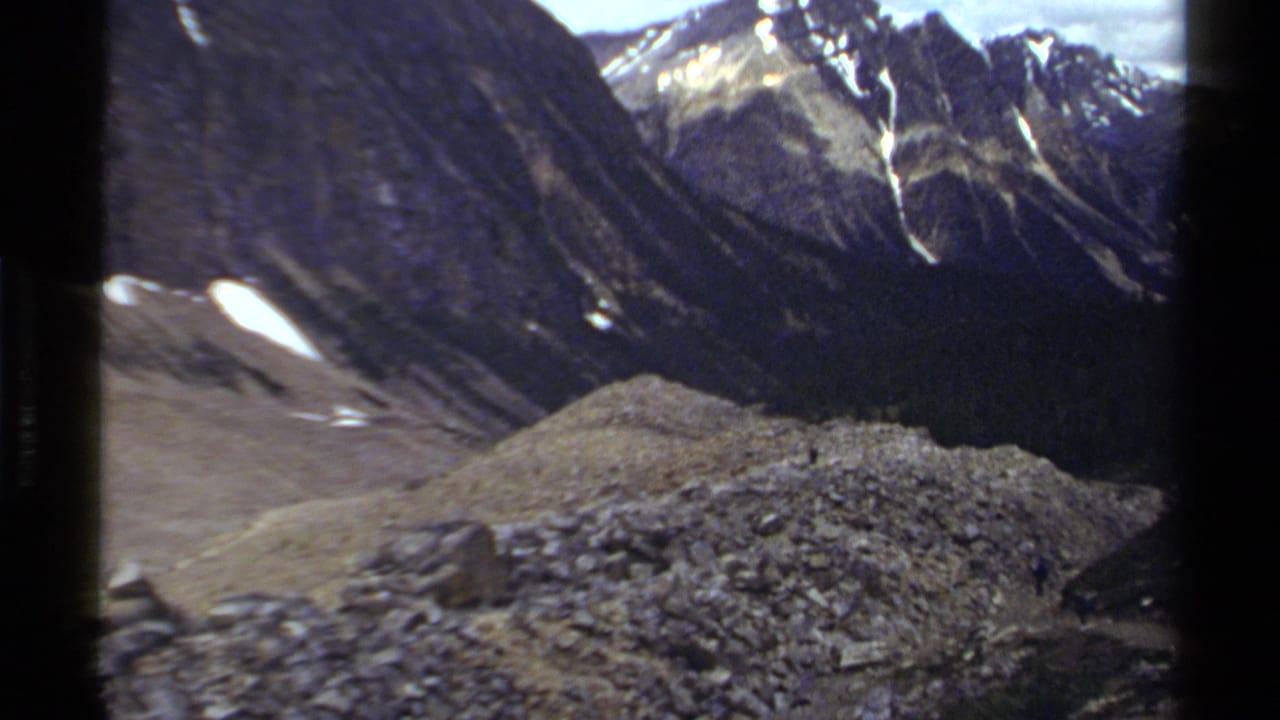 Rocky mountain slope with snow patches and dark ridges in the background.