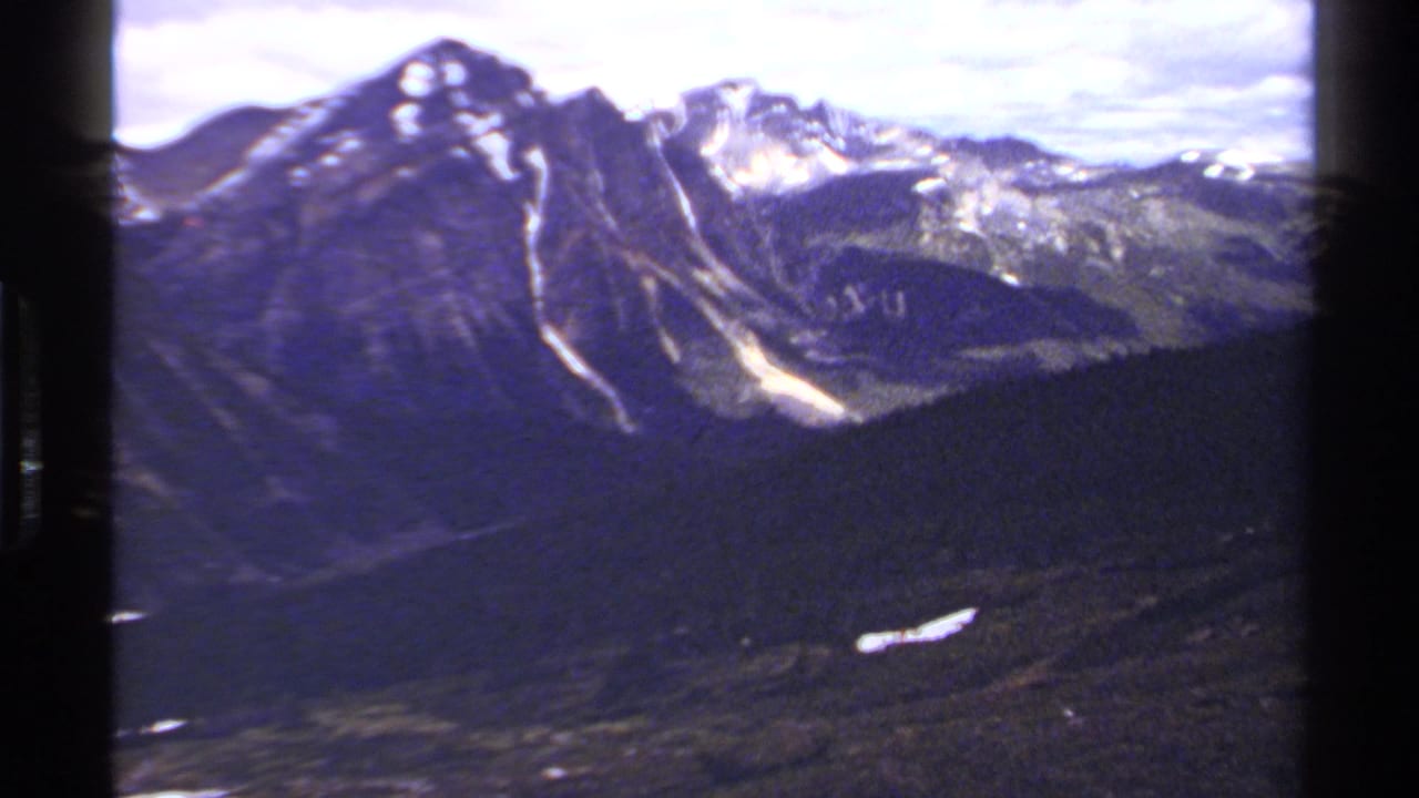 Snow-streaked mountain peaks above dark forested slopes under a cloudy sky.