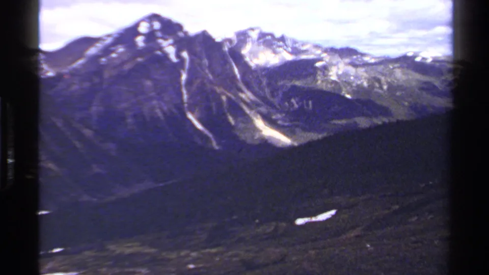 1979 8mm view of British Columbia mountain ridges with lingering snow, forested lower slopes, and dark film borders.