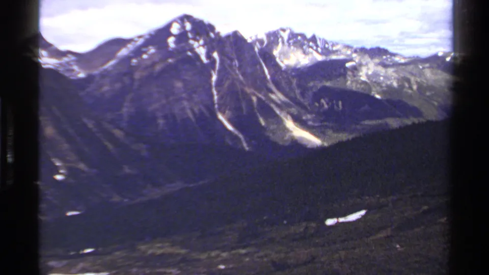 British Columbia alpine landscape on 8mm film, showing a snow-lined peak, adjacent ridges, and forested slopes.