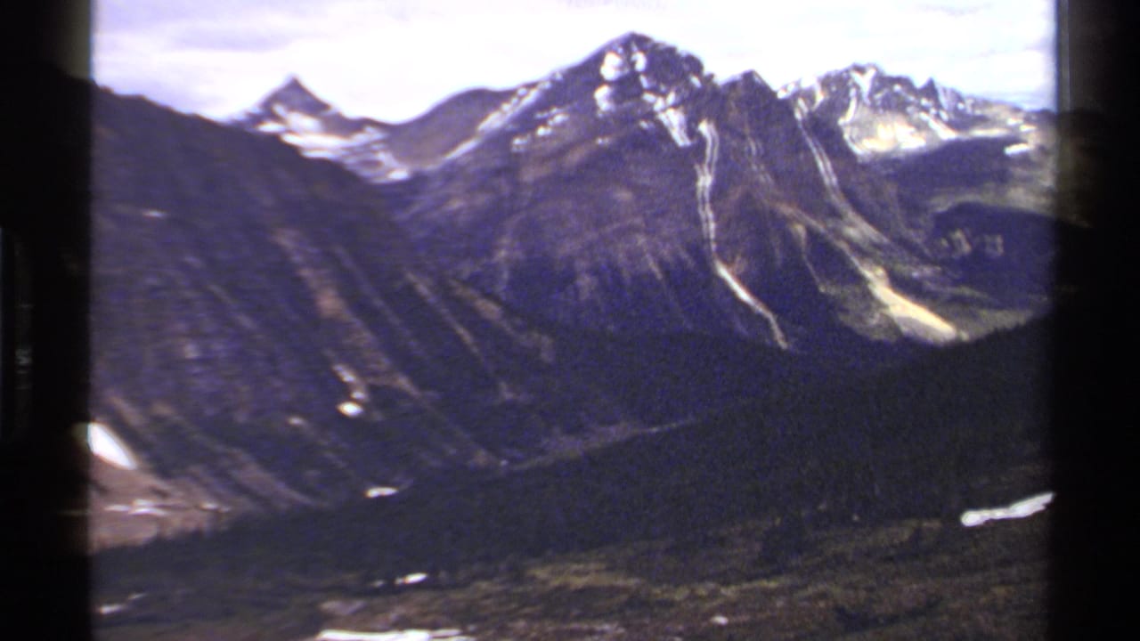 1979 8mm view of British Columbia mountains with snow patches, rocky ridges, forested slopes, and valley terrain.