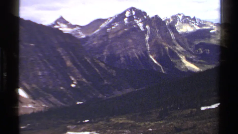 1979 8mm view of British Columbia mountains with snow patches, rocky ridges, forested slopes, and valley terrain.