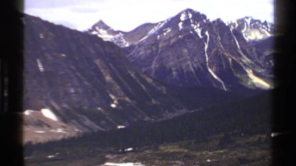 British Columbia mountain landscape on 8mm film, showing rugged peaks, snow patches, and a forested valley below.
