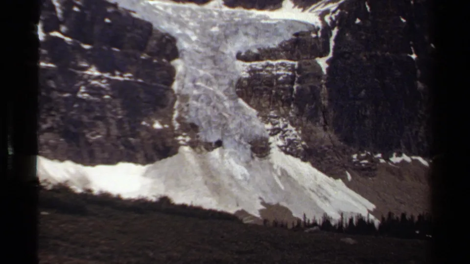 British Columbia mountain terrain on 8mm film, showing a snow-streaked rock face and pale scree slope.