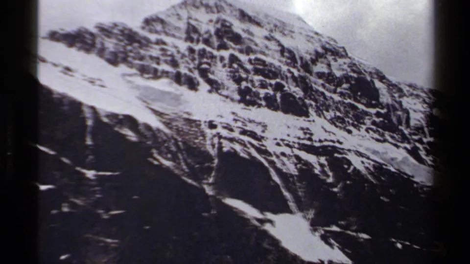 1979 British Columbia home-movie frame of a jagged mountain peak with snow fields across dark rock.