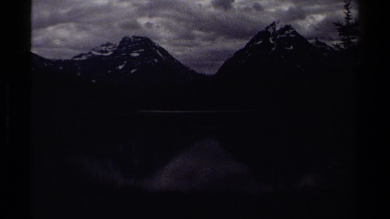 Dark exposed 8mm frame of mountain peaks over a lake under a cloudy sky.