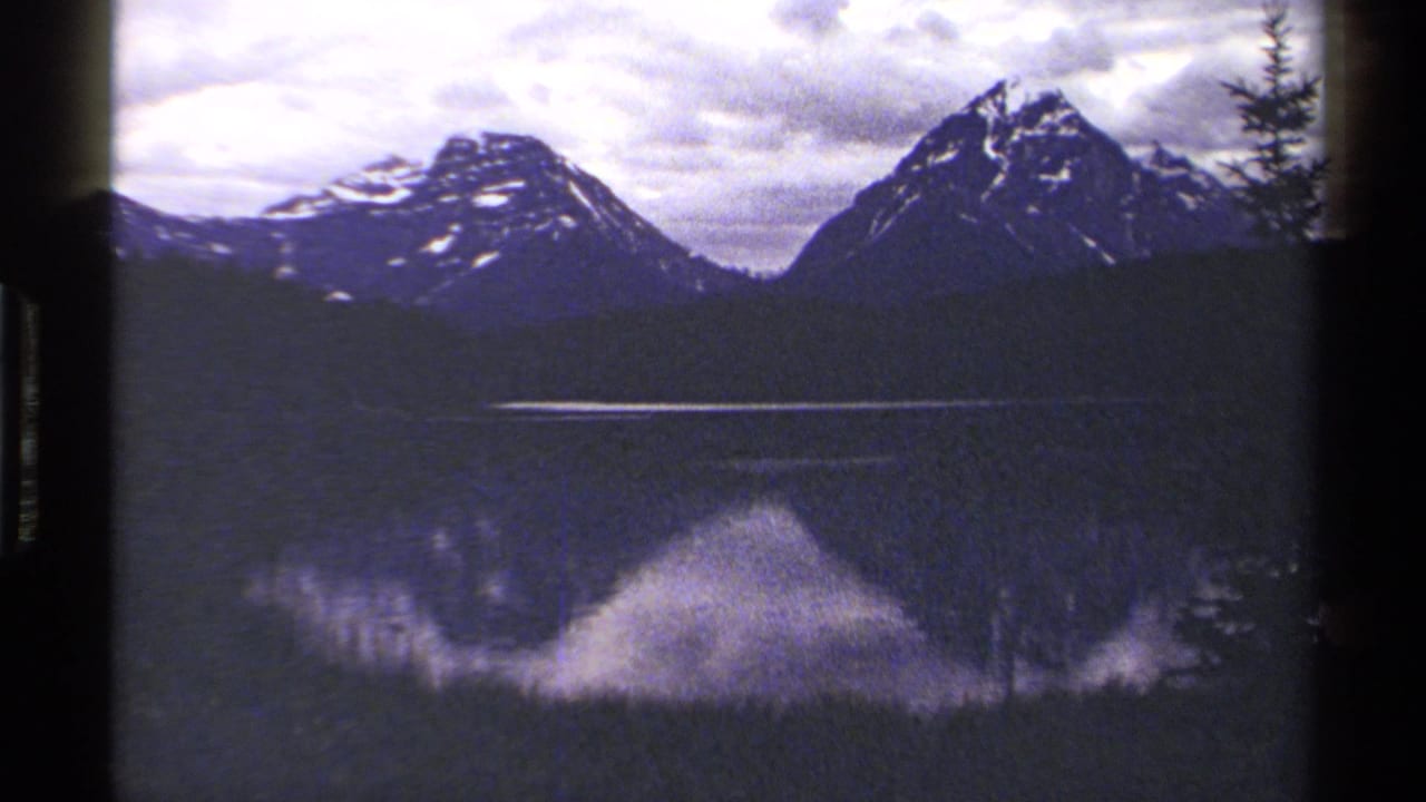 1979 British Columbia 8mm frame of blue-toned mountain peaks over a calm reflective lake, bordered by dark exposed film edges.