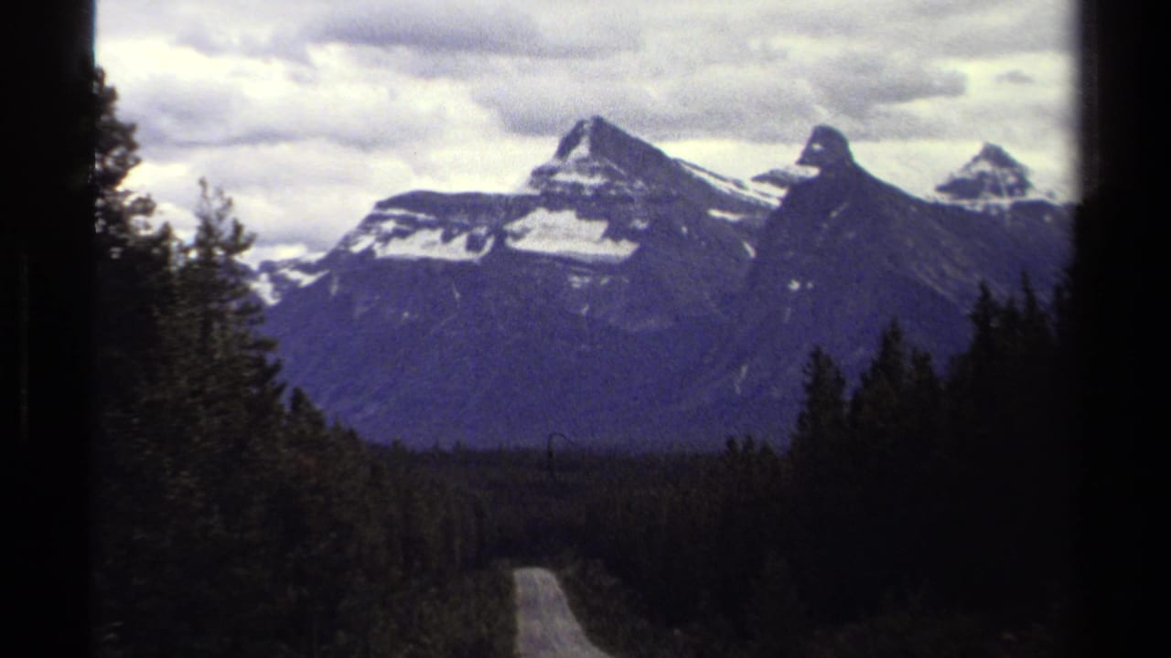 Distant mountain peaks above a dark evergreen forest with a road below.