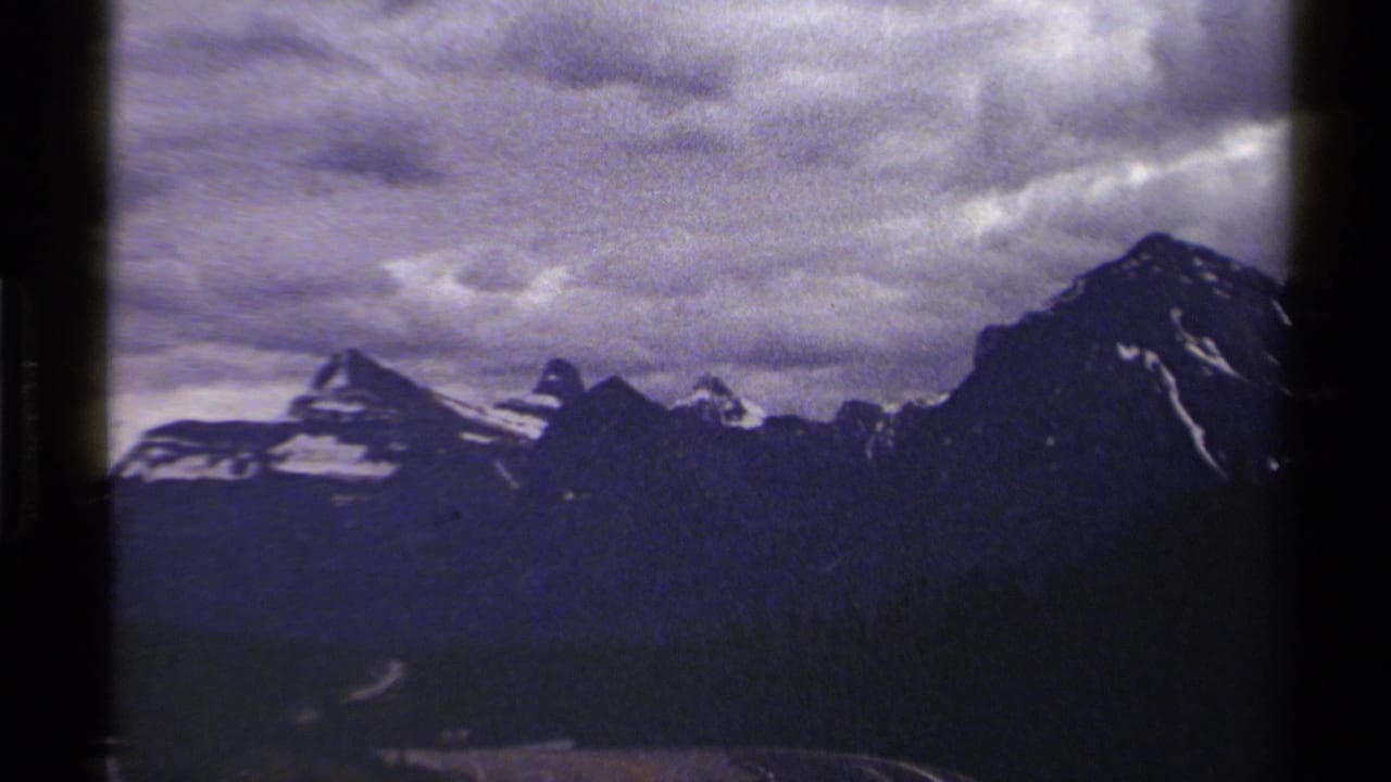 1979 8mm British Columbia mountain view with snow patches on rugged peaks beneath layered clouds.