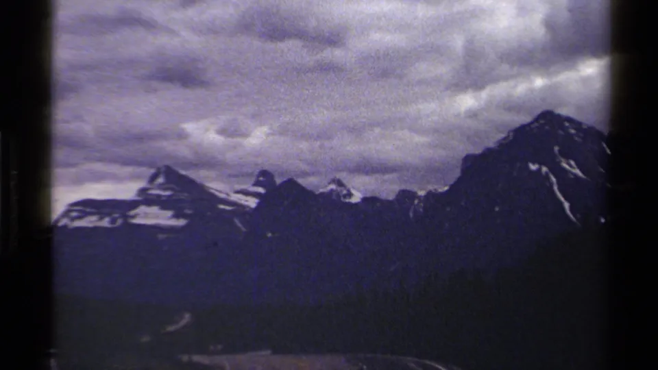 1979 8mm British Columbia mountain view with snow patches on rugged peaks beneath layered clouds.