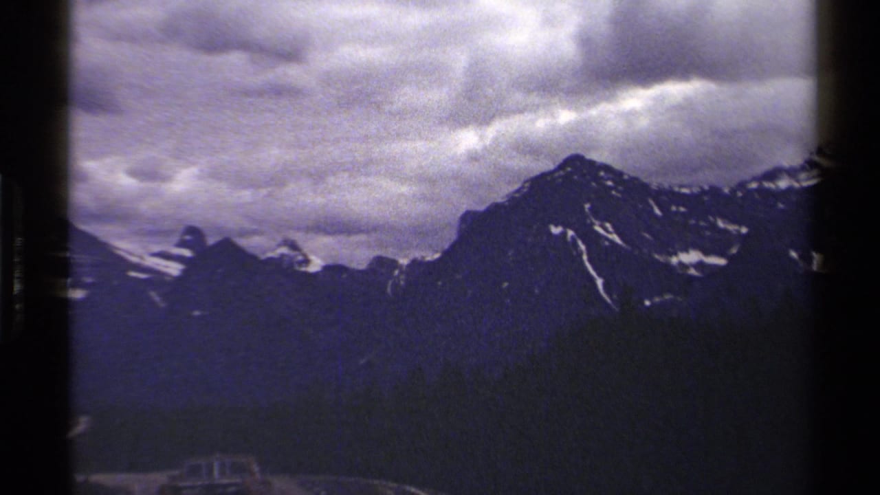 A steady 8mm pan across British Columbia alpine ridges, with snow traces and a cloudy sky.